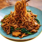 Chinesische gebratene Nudeln mit Hähnchenfleisch angerichtet auf einem Teller