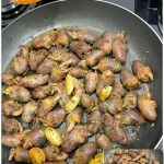 Gebratene Hähnchenherzen mit Knoblauch und frischen Kräutern auf einem Teller.