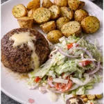 Rinderfrikadelle mit Ofenkartoffeln und Krautsalat auf einem Teller serviert