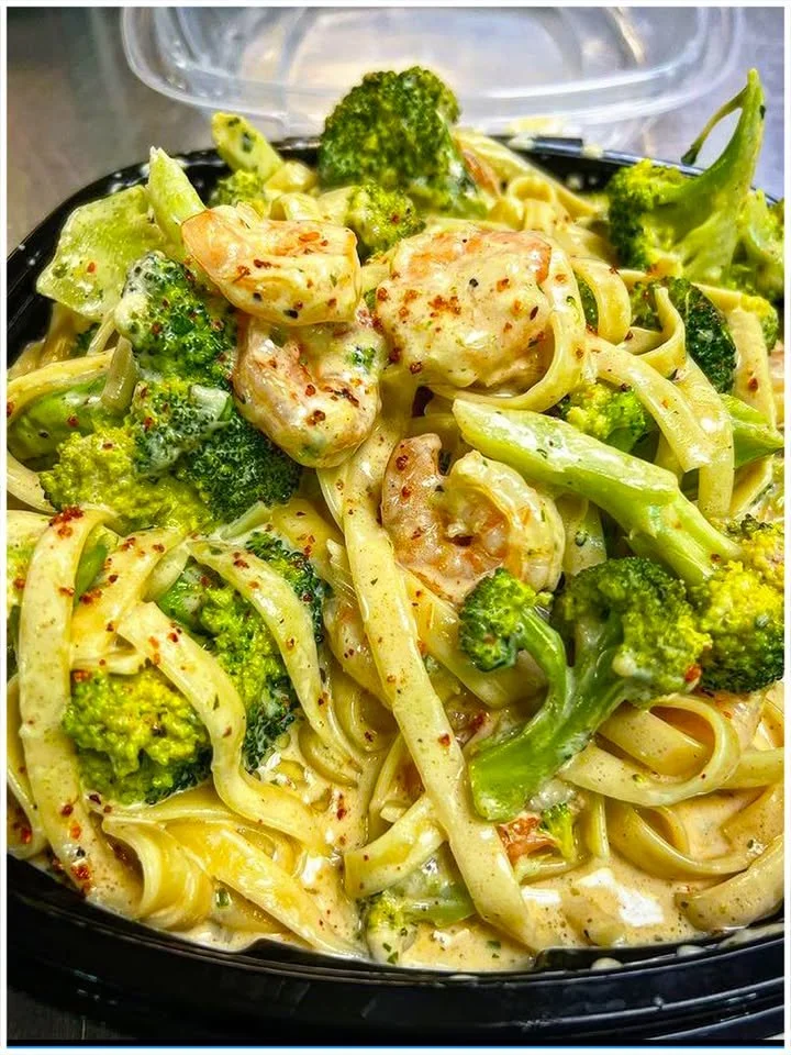 Tagliatelle mit Brokkoli und Garnelen in cremiger Sauce serviert in einem weißen Teller.