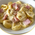Tortellini in Schinken-Käse-Sahnesauce auf einem Teller angerichtet.