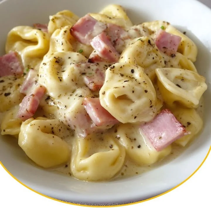 Tortellini in Schinken-Käse-Sahnesauce auf einem Teller angerichtet.