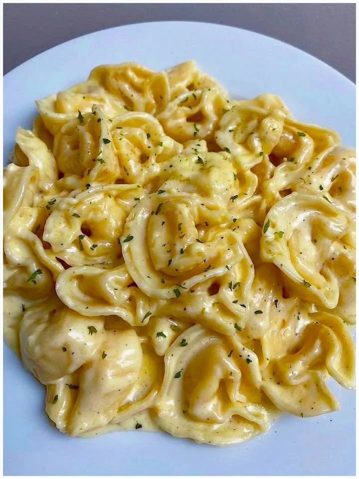 Tortellini mit Sahne in einer Schüssel, garniert mit frischen Kräutern