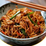 Ein Teller mit chinesischen Bratnudeln, bunt garniert mit Gemüse und Soße.