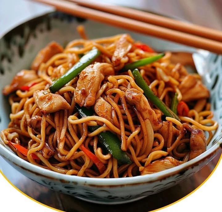 Ein Teller mit chinesischen Bratnudeln, bunt garniert mit Gemüse und Soße.